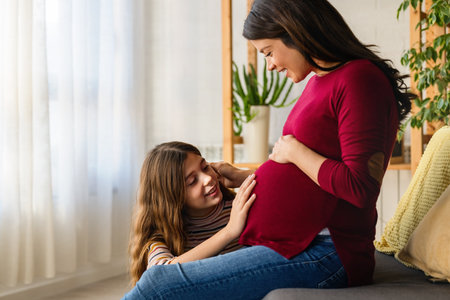 Lovely daughter touching mothers pregnant belly. Happy little girl feeling baby at mother tummyの写真素材