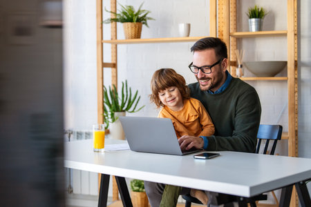 Father with kid having fun online with application watching video cartoons or playing game on laptopの写真素材