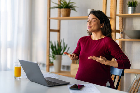 Pregnant woman using online app to practice breathing exercise while working from home.の写真素材