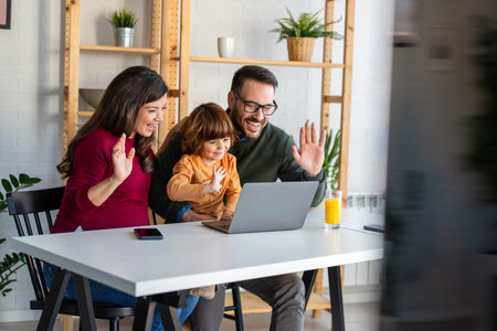 Parents and child relaxing at home with computer watching funny internet video, making online callの写真素材