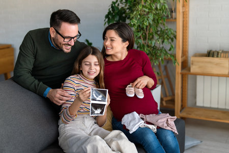 Cozy family time at home as pregnant mom, dad, and daughter enjoy shared moments on the sofaの写真素材
