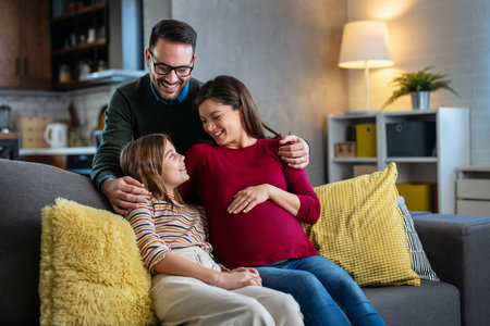 Happy family with pregnant mother sitting on sofa, having fun with joyful kid, waiting for babyの写真素材