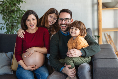 Loving husband and children hugging pregnant mother, touching her belly. Happy, excited familyの写真素材