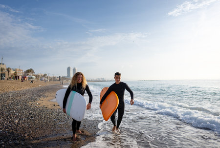 Beautiful happy surfer couple having fun on the beach, running with surfboard to the wavesの写真素材