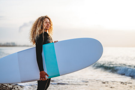 Joyful young woman carrying a surfboard on a beach, her face filled with happiness and excitementの写真素材