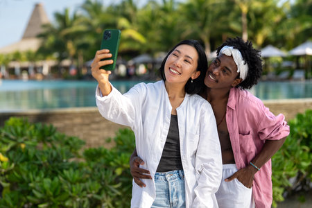 Trendy digital creator couple taking selfie by the beach, sharing travel content for social mediaの写真素材