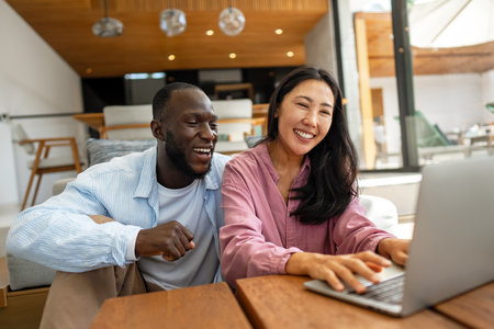 Happy young diverse, multiethnic couple planning budget, reading good news on laptop at homeの写真素材