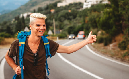 Young Caucasian man hitchhiking standing by road on sunny summer dayの写真素材