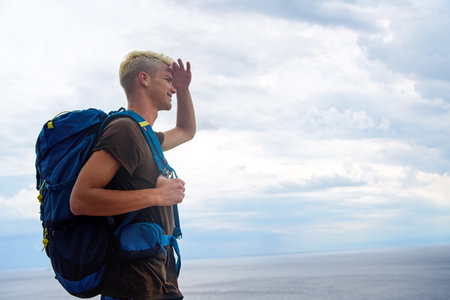 Young man traveler and explorer is hiking the hill. Overlooking sea, ocean and hills on the horizonの写真素材