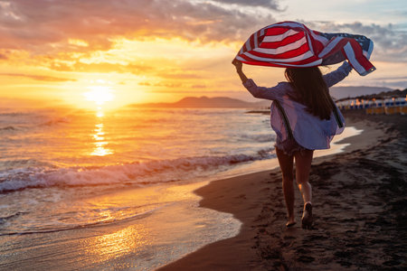Happy woman smiling and running on beach with the US flag. July 4th independence day. Holidayの写真素材