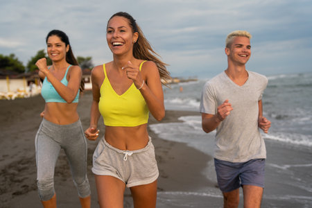 Group of young people, friends in sports clothing jogging while exercising on the beach outdoorsの写真素材