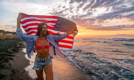 Young woman holding national American flag walking ocean beach. America Independence Day conceptの写真素材