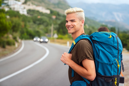 Young Caucasian man hitchhiking standing by road on sunny summer day.の写真素材
