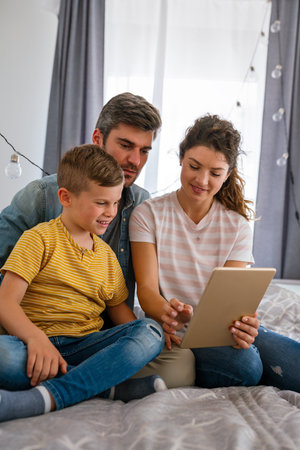 Happy family with kid having fun using tablet together, parents and child laughing relaxing at homeの写真素材