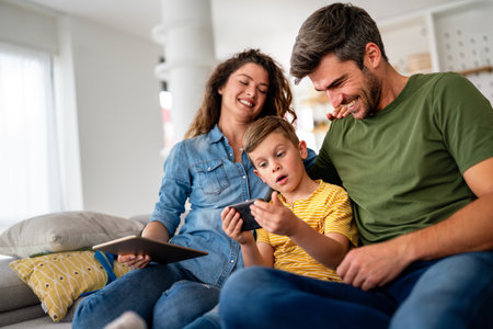 Happy family parents and kid use laptop phone digital tablet at homeの写真素材
