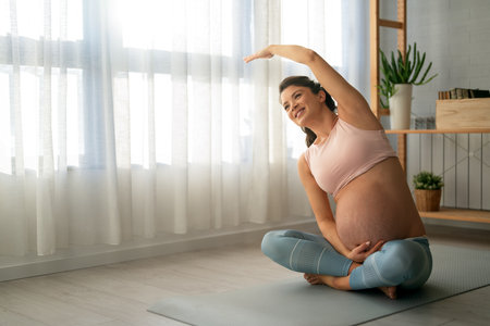 Portrait of young pregnant female working out at home. Pregnant woman practicing yoga at home.の写真素材