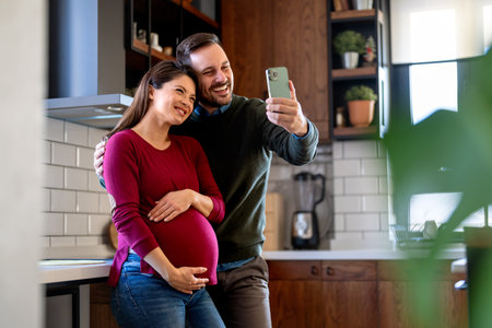 Pregnancy, technology and people concept. Happy man and his pregnant wife with smartphones at homeの写真素材