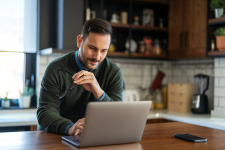 Satisfied man using laptop computer for electronic banking, making reservation, online shoppingの写真素材