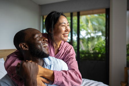 Excited multiethnic couple embracing and laughing in modern living room, calm lifestyleの写真素材