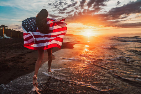 Happy woman smiling and running on beach with the US flag. July 4th independence day. Holidayの写真素材