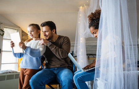 Happy father in wheelchair with interracial daughters using laptop together, education, fun conceptの写真素材