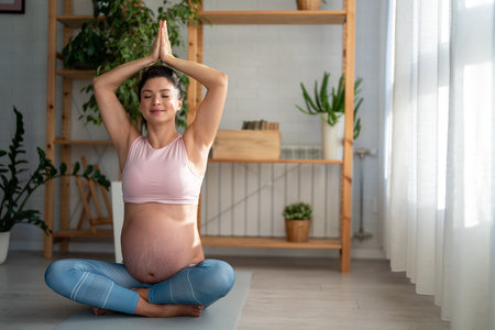 Relaxed pregnant woman doing breathing exercises while sitting on an exercise mat at homeの写真素材