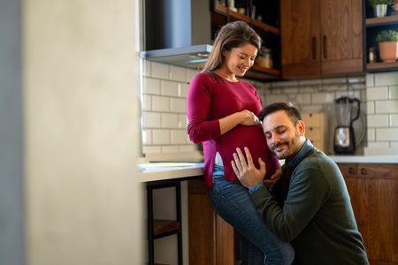 Beautiful pregnant woman and her handsome husband are smiling while spending time togetherの写真素材