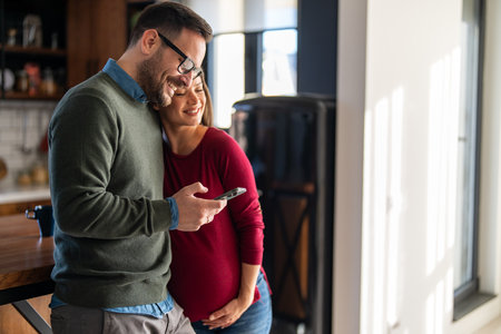Pregnancy, technology and people concept. Happy man and his pregnant wife with smartphones at homeの写真素材