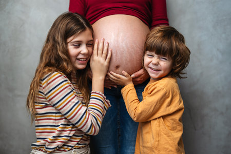 Lovely children touching mothers pregnant belly. Happy little siblings feeling baby at mother tummyの写真素材