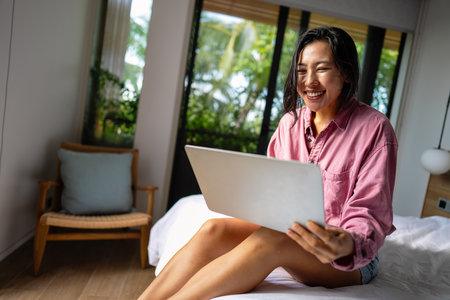 Middle eastern, asian woman managing her online banking, social life, and tasks on a laptopの写真素材