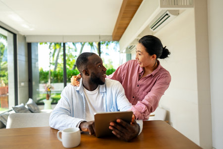Young happy multiethnic couple having fun while using tablet at home. Happy couple discussing futureの写真素材