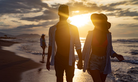 Happy young casual couple holding hands and walking at the beach, enjoying summer vacationの写真素材