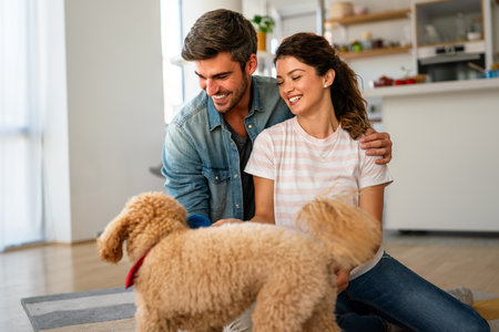 Happy couple playing with dog, having fun on floor at home. Married couple with cute petの写真素材