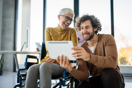 Business woman in wheelchair working with colleague in modern inclusive office. Diversity, supportの写真素材