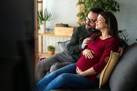 Beautiful young couple with pregnant wife at home with her husband touching his wifes belly