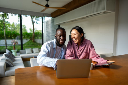 Overjoyed multiethnic couple using laptop, shopping online with sales, playing game togetherの写真素材