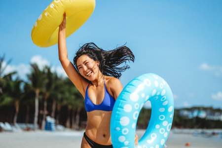 Young woman raises her hands with inflatable rings, celebrating the freedom of a beach vacationの写真素材