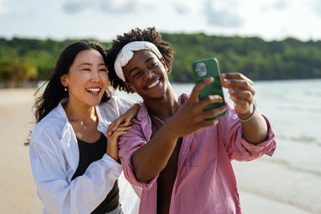 Happy interracial couple taking selfie at a tropical beach enjoying vacation, remote workの写真素材