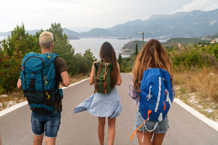 Happy friends on a road trip have fun, piggybacking at the roadside and enjoying summer vacation