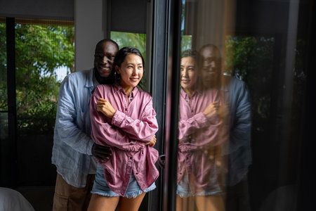 Young diverse couple joyfully smiling together in their bright living room, wearing casual clothesの写真素材