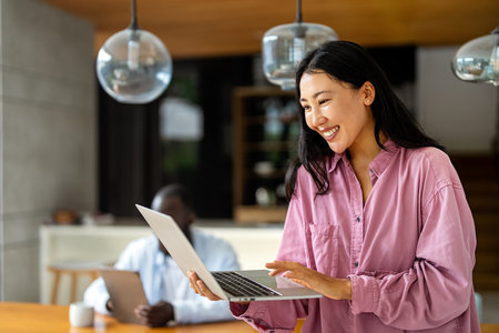 Middle eastern, asian woman working on a laptop in a tropical-inspired home officeの写真素材