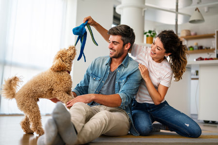 Happy couple playing with dog, having fun on floor at home. Married couple with cute petの写真素材