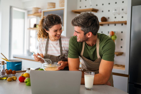 Young couple using laptop computer to take part in online culinary workshop, cooking togetherの写真素材