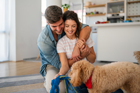 Portrait of happy multiracial couple scratching their pet dog, sitting on floor at home. Adopted petの写真素材