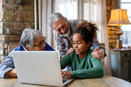 Happy senior couple using modern tech gadget laptop together with grandchild at home.