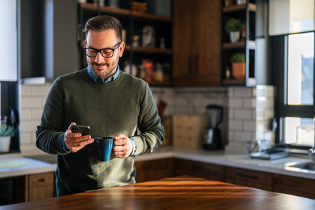Checking his messages over coffee. Man using a smart phone while drinking coffee at homeの写真素材