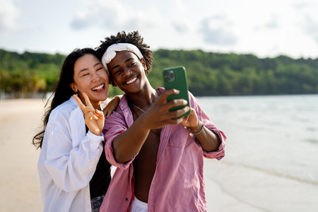 Trendy digital creator couple taking selfie by the beach, sharing travel content for social mediaの写真素材