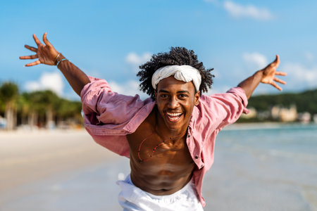 Young Black man enjoying a sunny beach day, running through ocean waves, smiling and feeling freeの写真素材