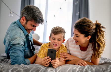 Happy parents with kid using smartphone at home together, playing, having fun with dog