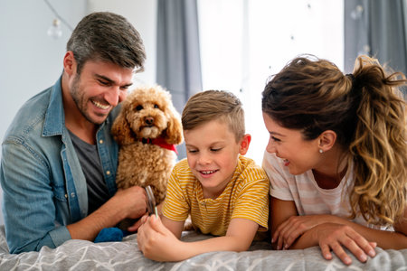 Happy parents with kid using smartphone at home together, playing, having fun with dogの写真素材